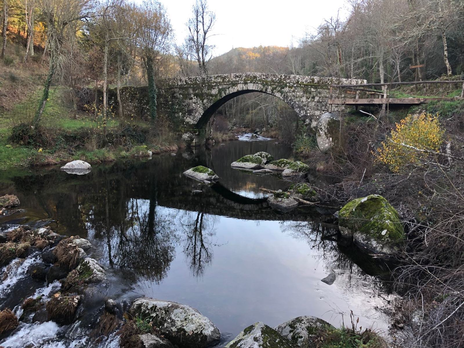 Ponte antiga de pedra sobre um rio de montanha, com águas calmas e penedos